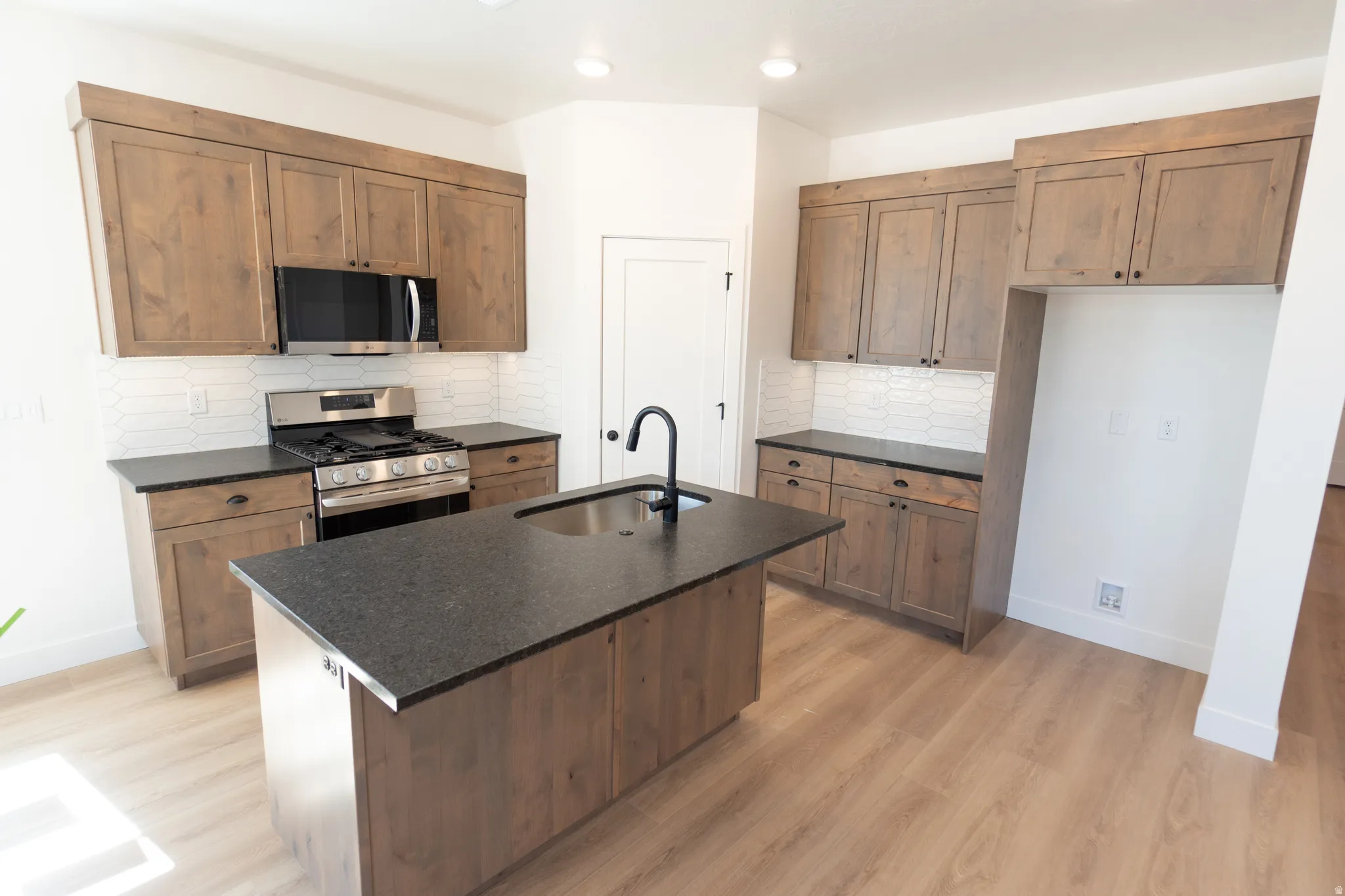Kitchen featuring wood-finish cabinetry, dark countertops, white subway tile backsplash, and wood-finish flooring