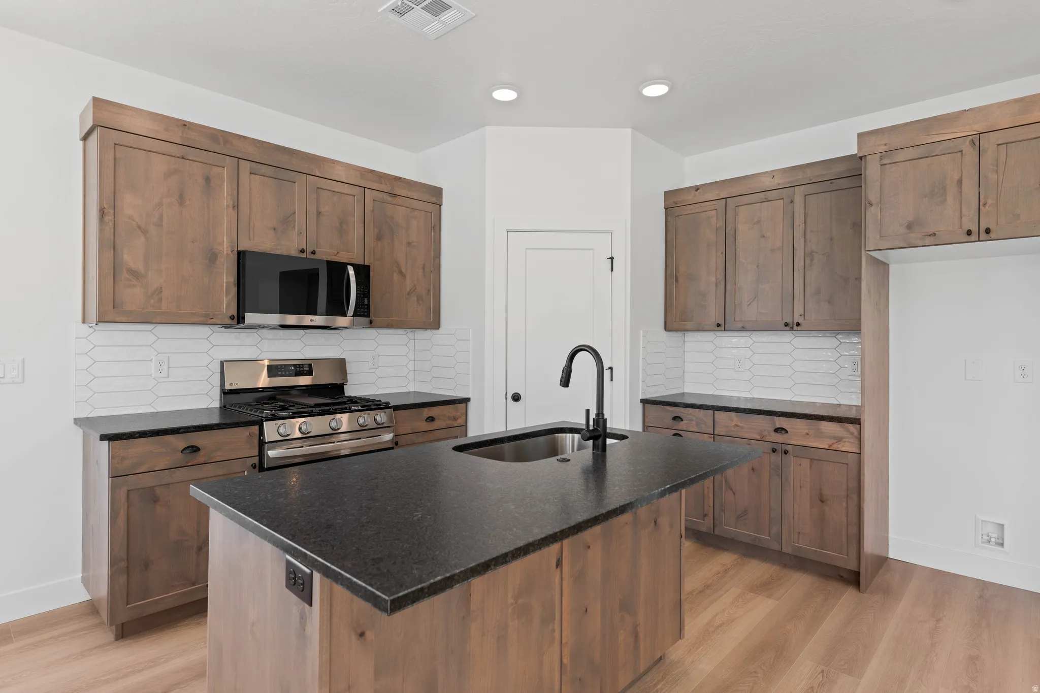 Kitchen featuring wood-finish cabinetry, black countertops, stainless steel appliances, and a central island with an integrated sink