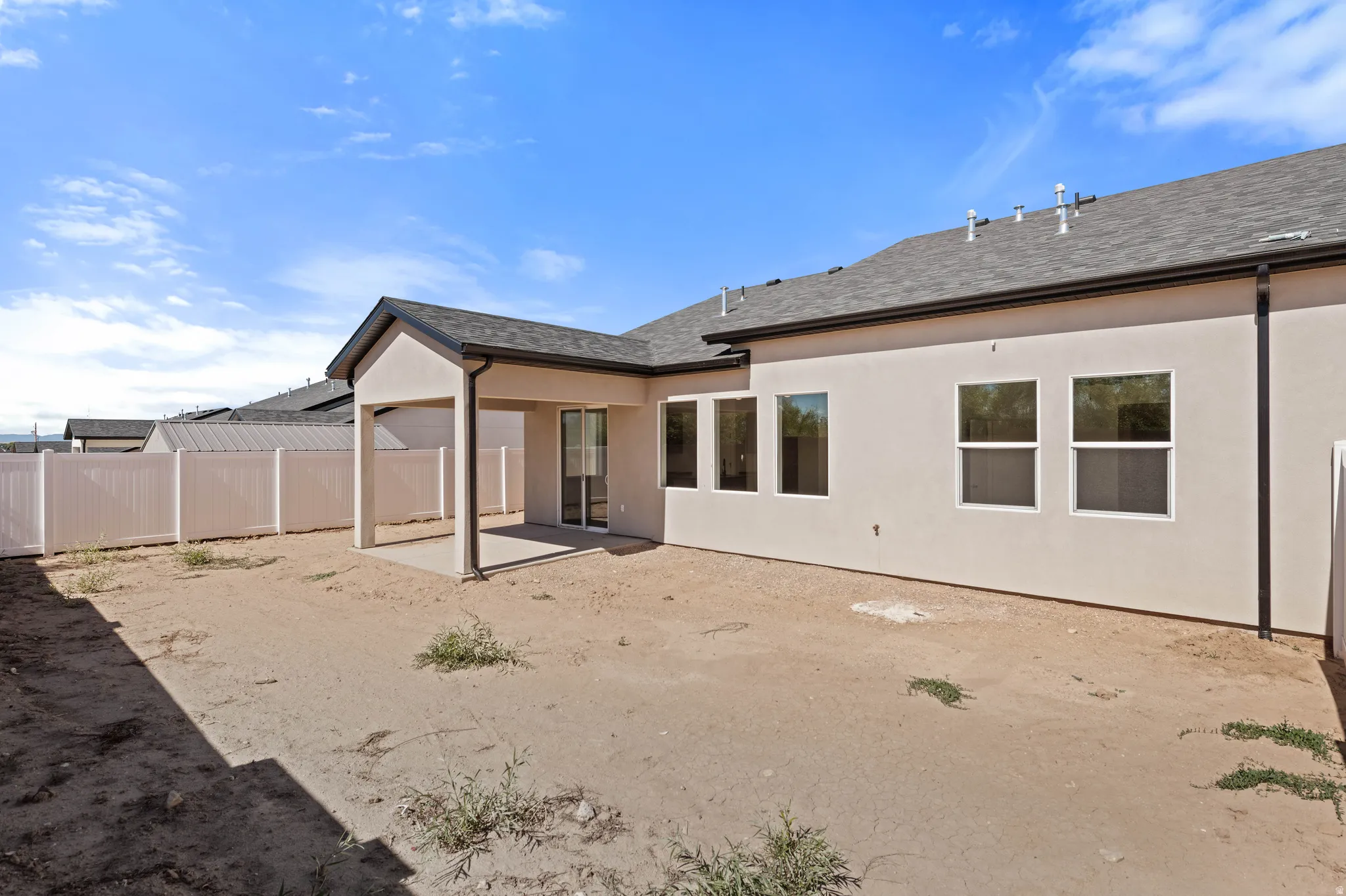 Rear exterior featuring stucco finish, multiple windows, a covered patio with concrete flooring, a sliding glass door, and a perimeter fence