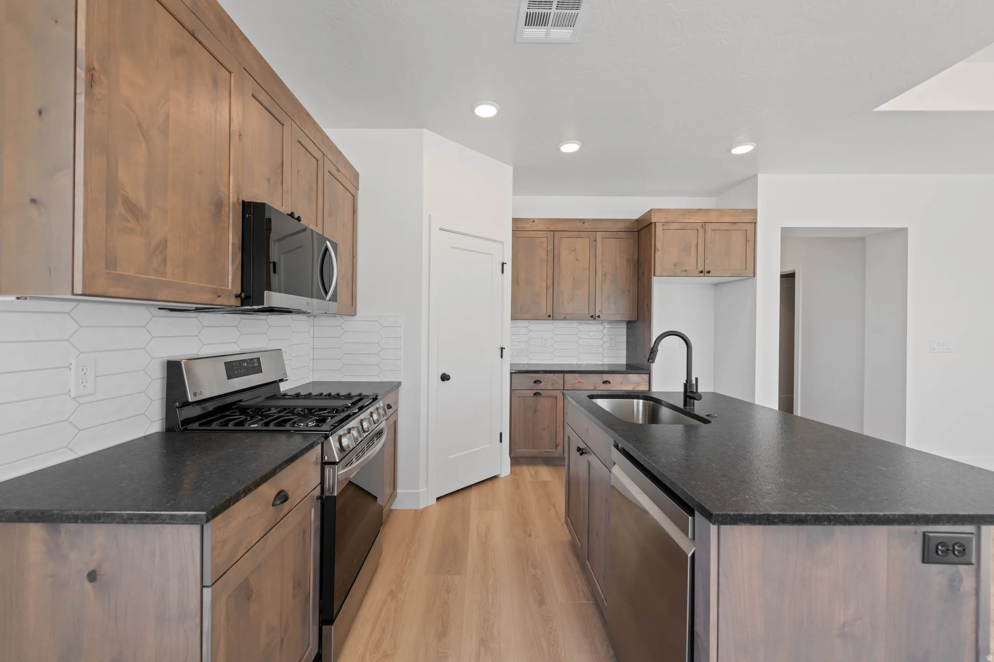 Kitchen featuring wood-finish cabinetry, dark countertops, a stainless steel gas range, and a kitchen island with an undermount sink and a matte black faucet