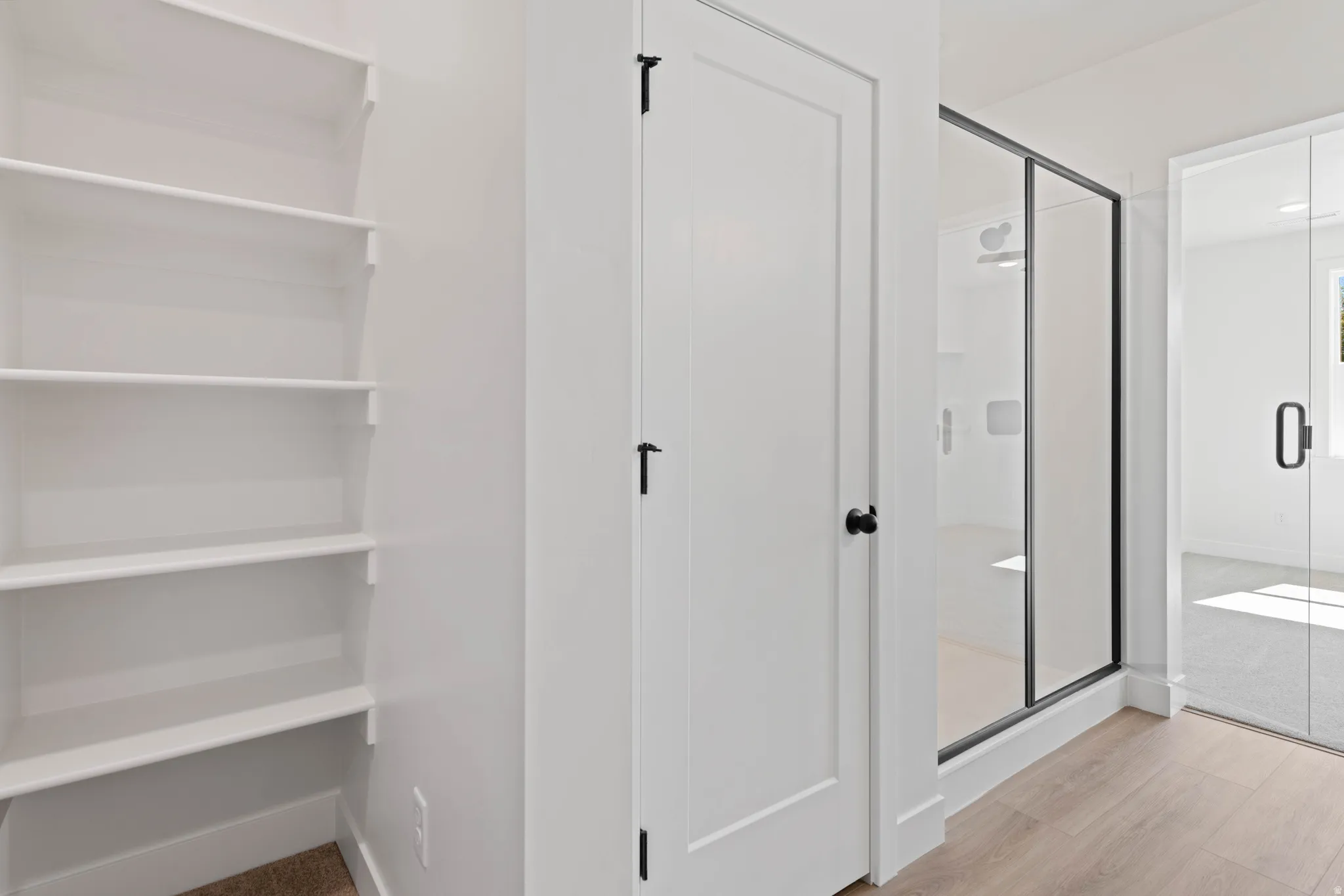 Built-in shelving, white paneled doors, matte black door hardware, glass-enclosed shower with black trim, and wood-finish flooring