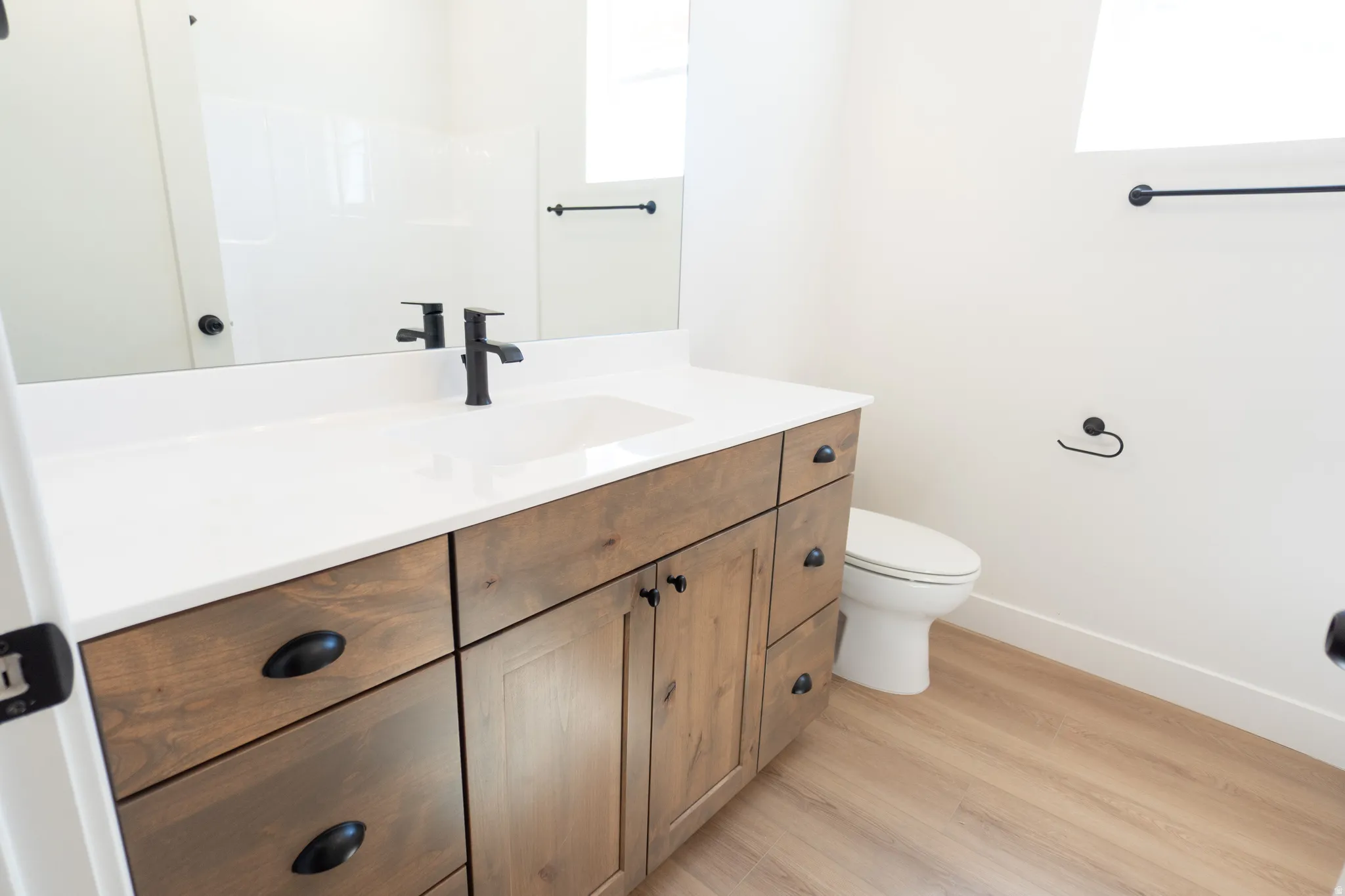 Wood-finish vanity with matte black hardware, white countertop, and integrated sink