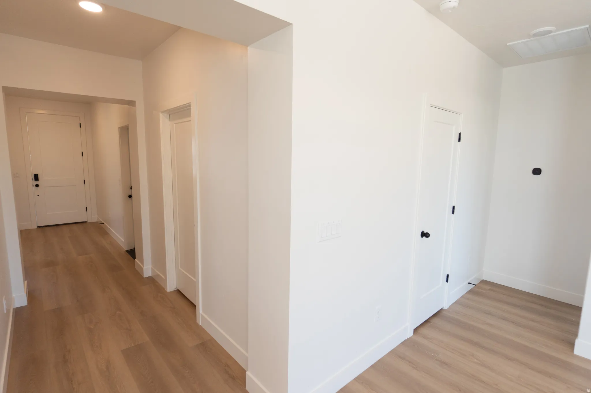 Light wood-finish flooring throughout, white interior doors with black hardware, recessed ceiling lighting, and crisp white wall finishes