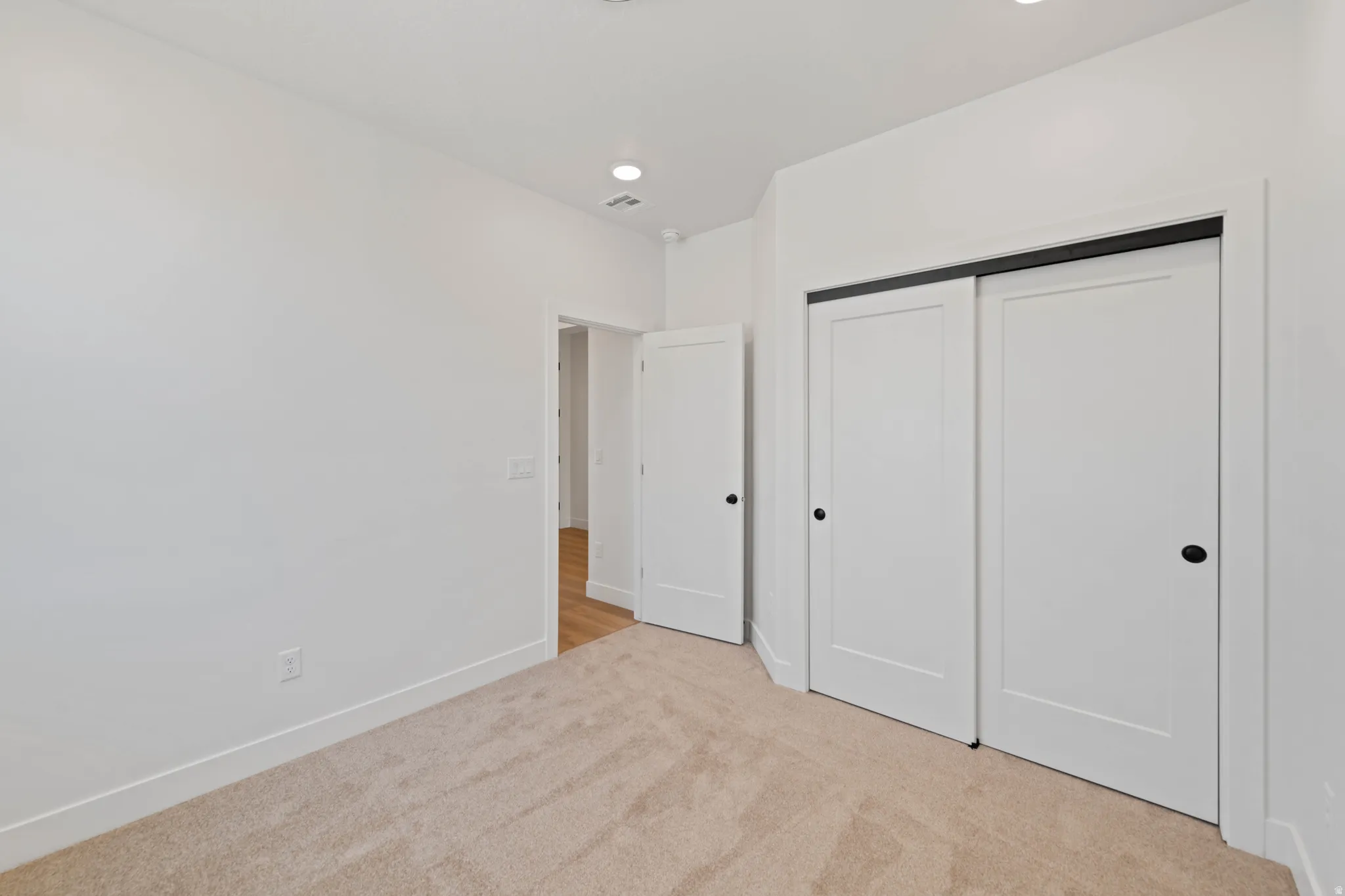 Plush carpet flooring, recessed lighting, white walls, white sliding closet doors, and a white interior door with black hardware