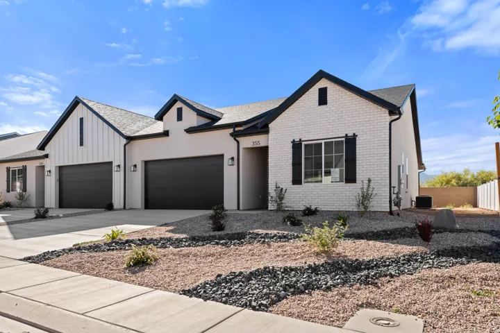 Contemporary exterior with white brick and stucco finishes, black trim, a gabled roofline, and attached two-car garages with dark doors