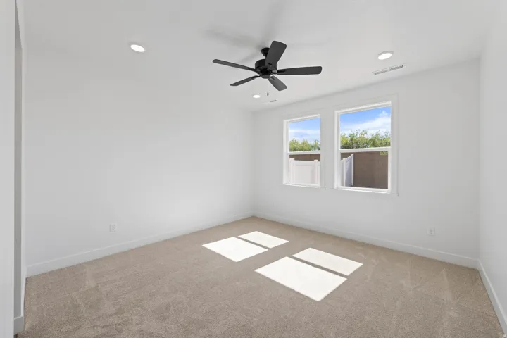 Recessed lighting, ceiling fan, white walls, two windows, and carpeting