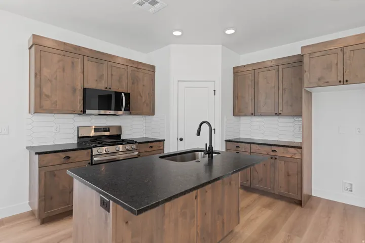 Kitchen featuring wood-finish cabinetry, black countertops, stainless steel appliances, and a central island with an integrated sink