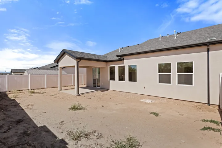 Rear exterior featuring stucco finish, multiple windows, a covered patio with concrete flooring, a sliding glass door, and a perimeter fence