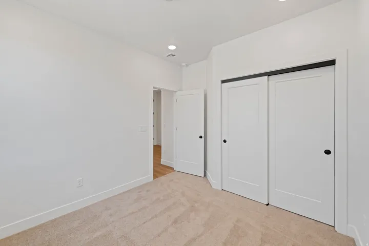 Plush carpet flooring, recessed lighting, white walls, white sliding closet doors, and a white interior door with black hardware