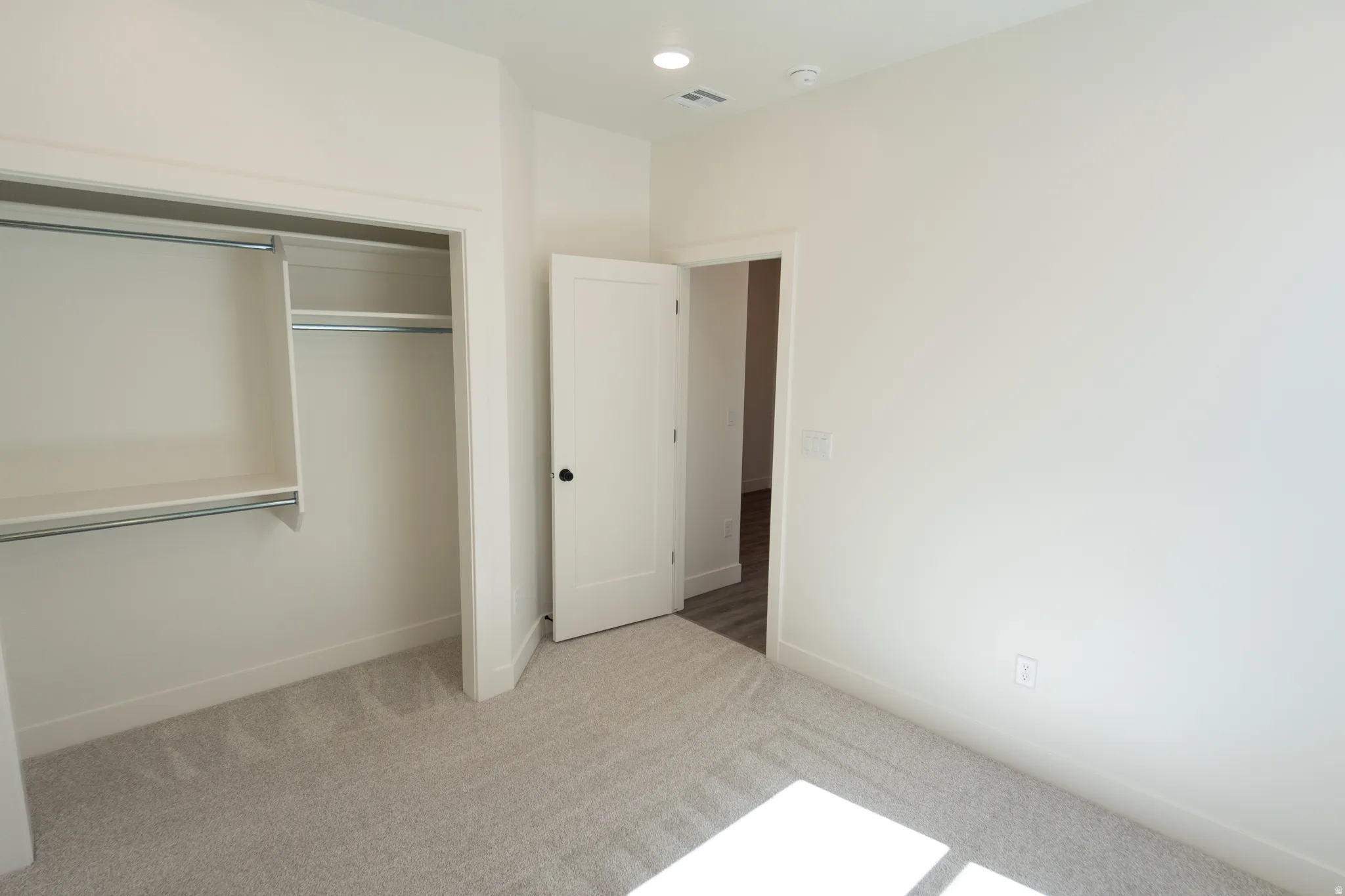 Soft gray carpet flooring paired with white walls, a single-panel interior door with matte black hardware, recessed lighting, and a closet with integrated shelving and hanging rods