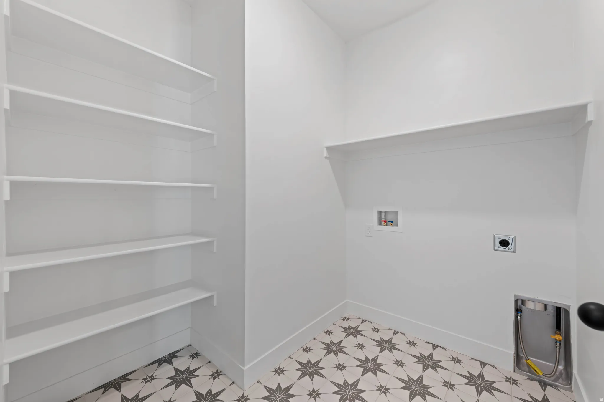 Laundry area featuring patterned floor tiles, white walls, built-in shelving, and utility hookups