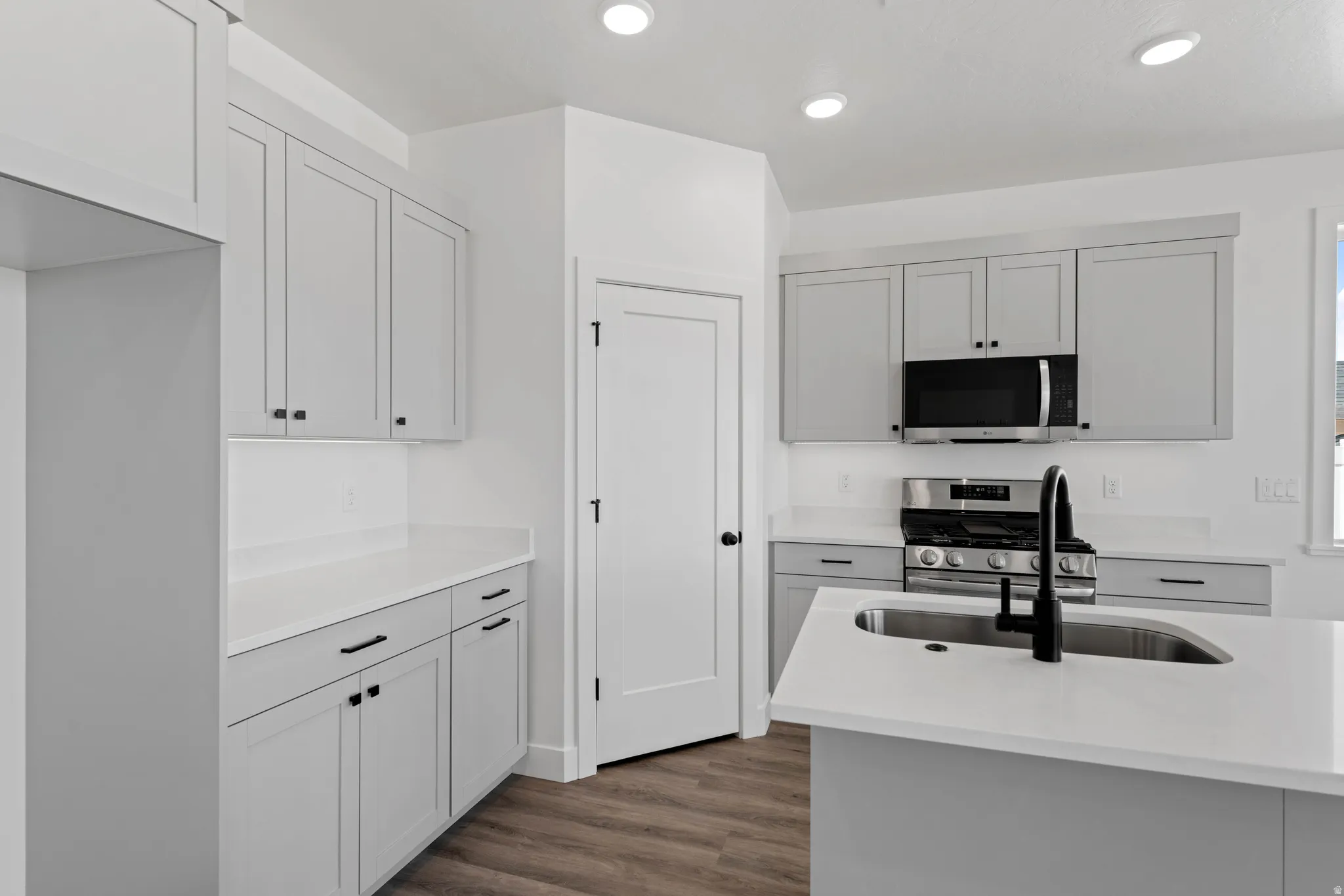 Contemporary kitchen featuring light gray cabinetry, white countertops, stainless steel appliances, and wood-finish flooring