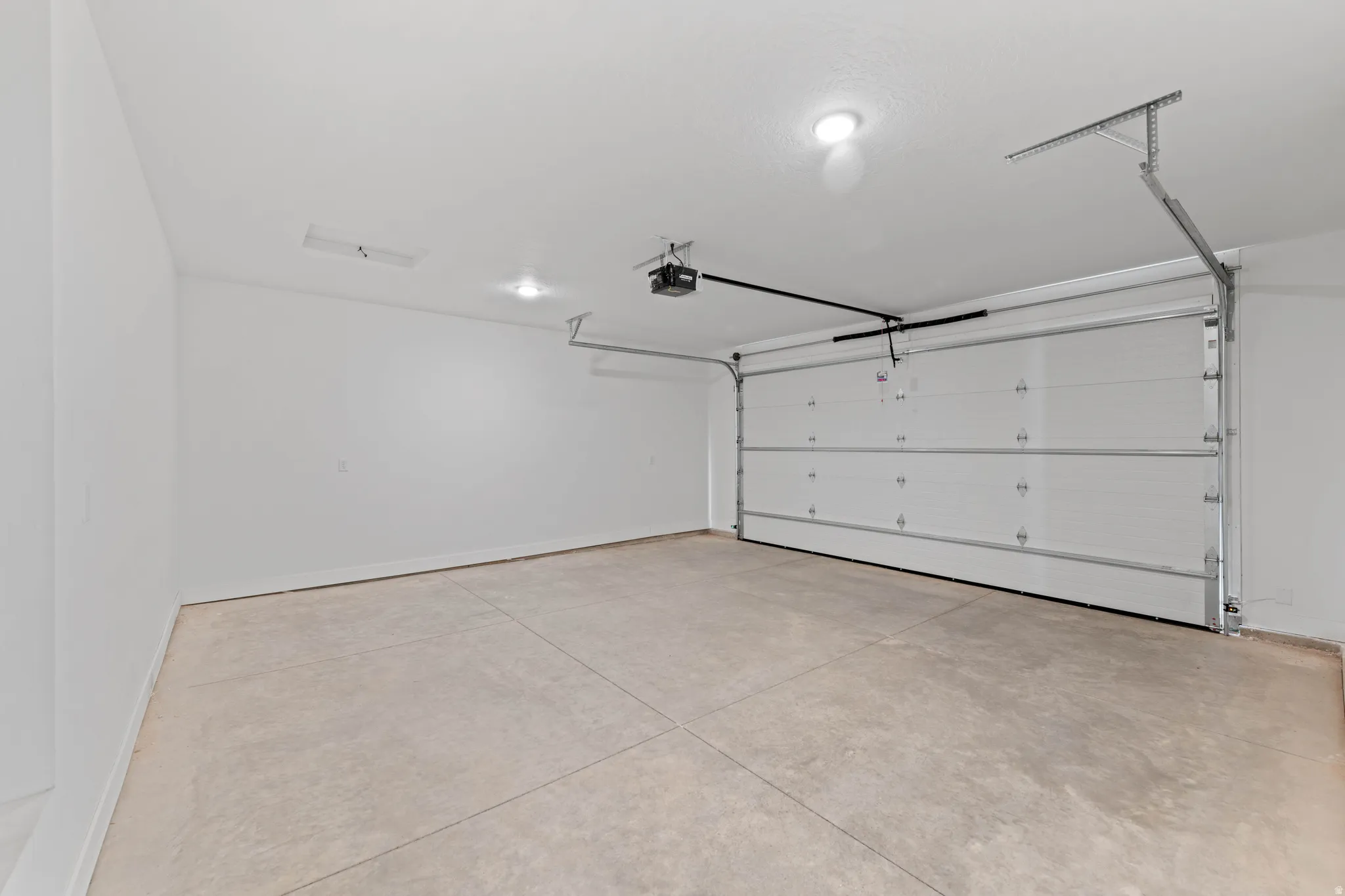 Attached garage with a white sectional door, concrete flooring, and ceiling-mounted lighting