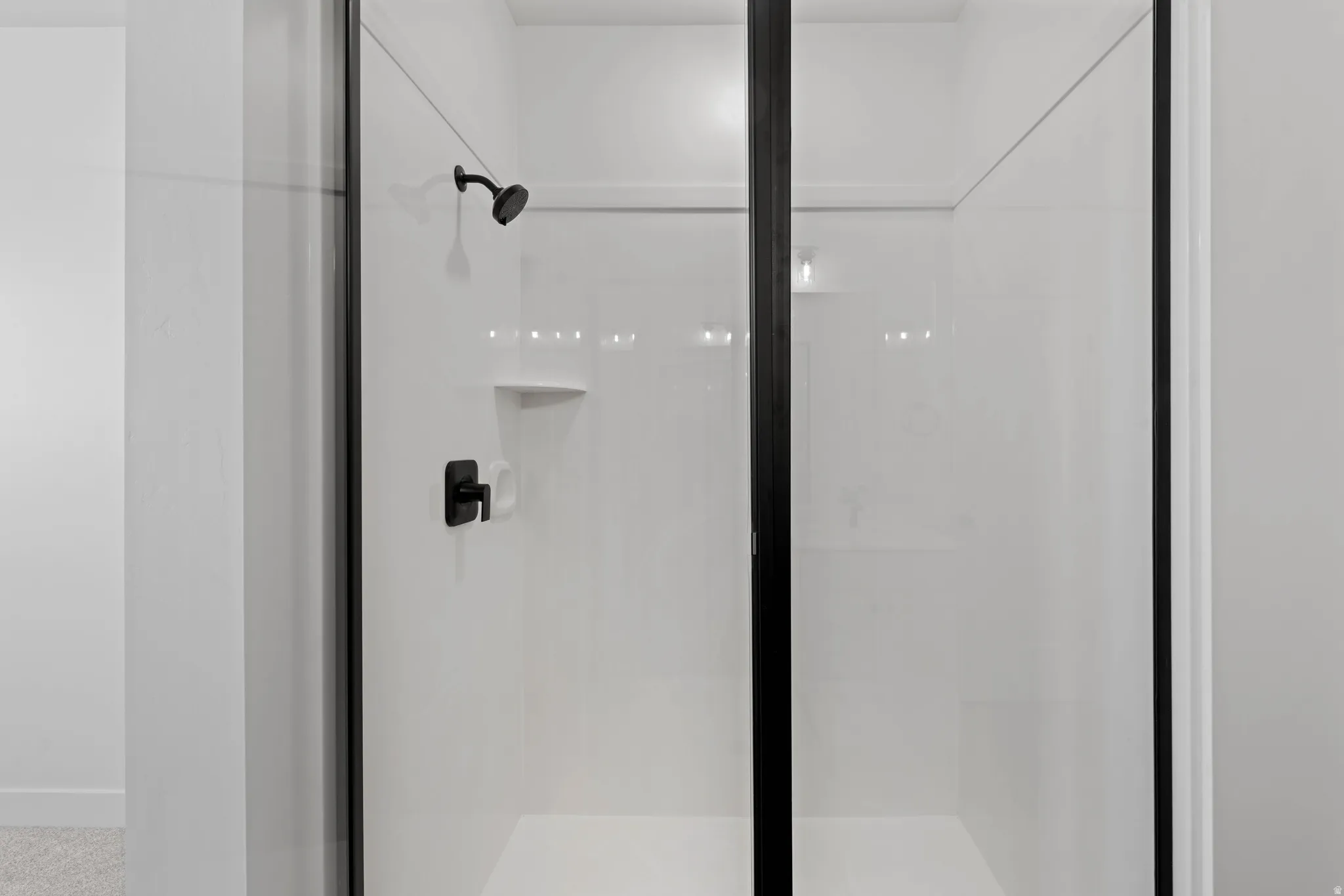 Shower enclosure with black-framed glass, white shower surround, matte black shower head, and matte black shower control