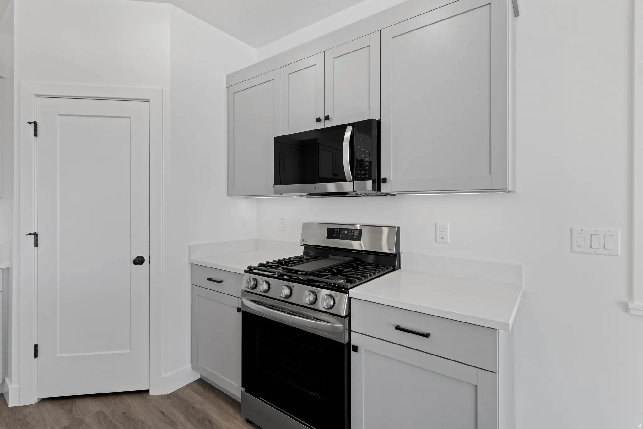 Stainless steel oven with gas cooktop, microwave, and range hood, light gray cabinetry with black hardware, white countertops, and wood-finish flooring