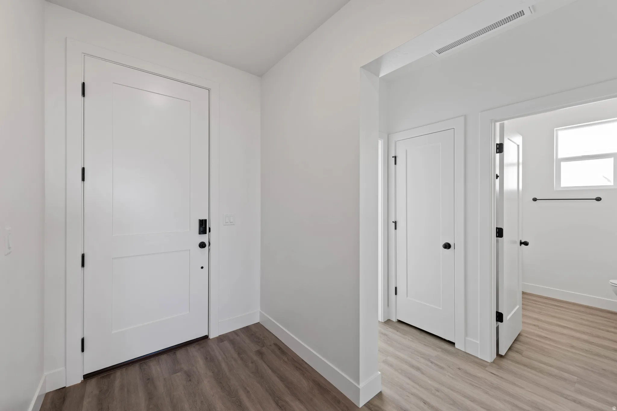 White interior doors, wood-finish flooring, matte black door hardware, white walls, and a window with natural light