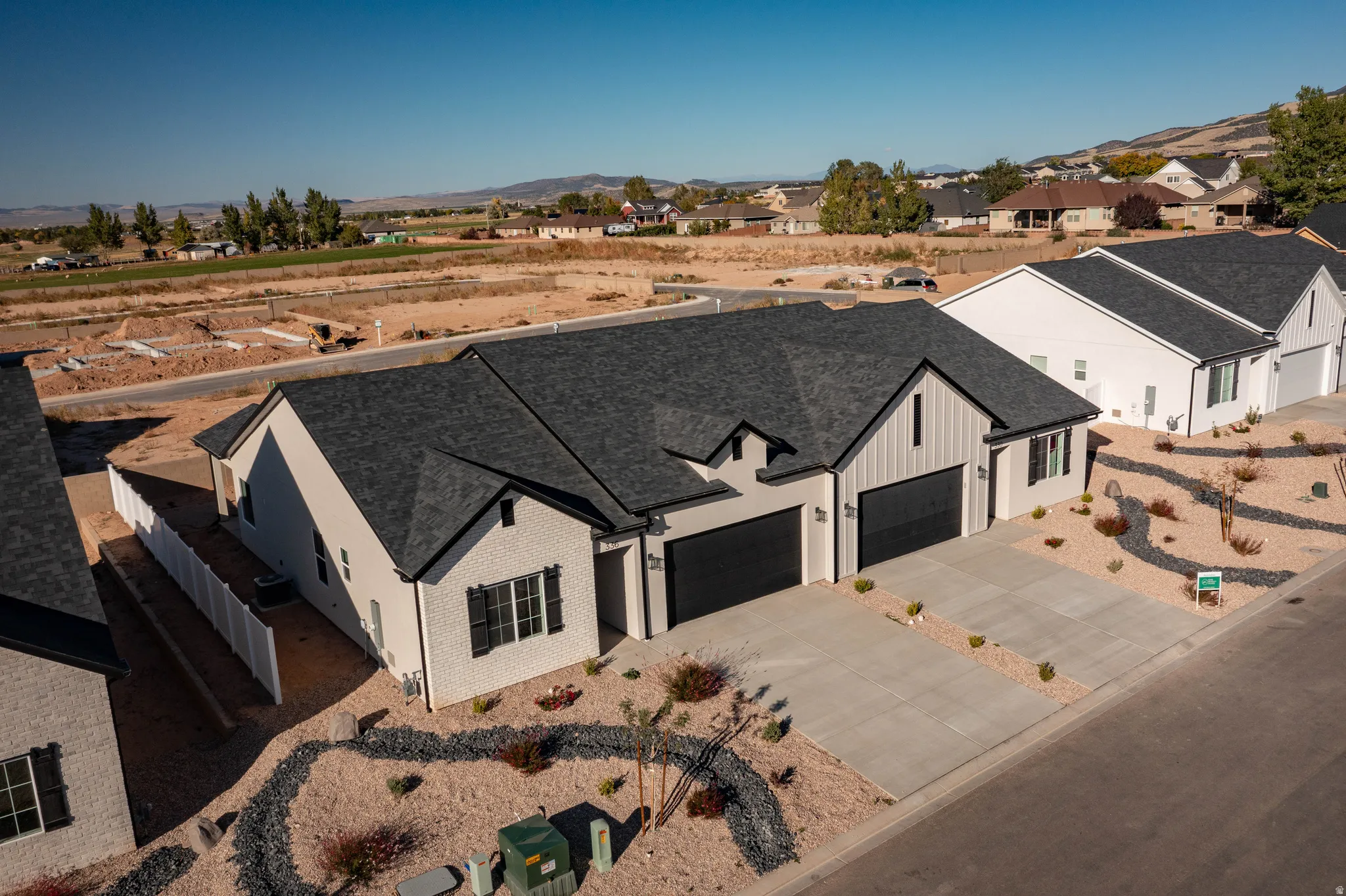Contemporary exterior featuring a dark gray shingle roof, light-colored brick facade, black garage doors, and decorative black window shutters