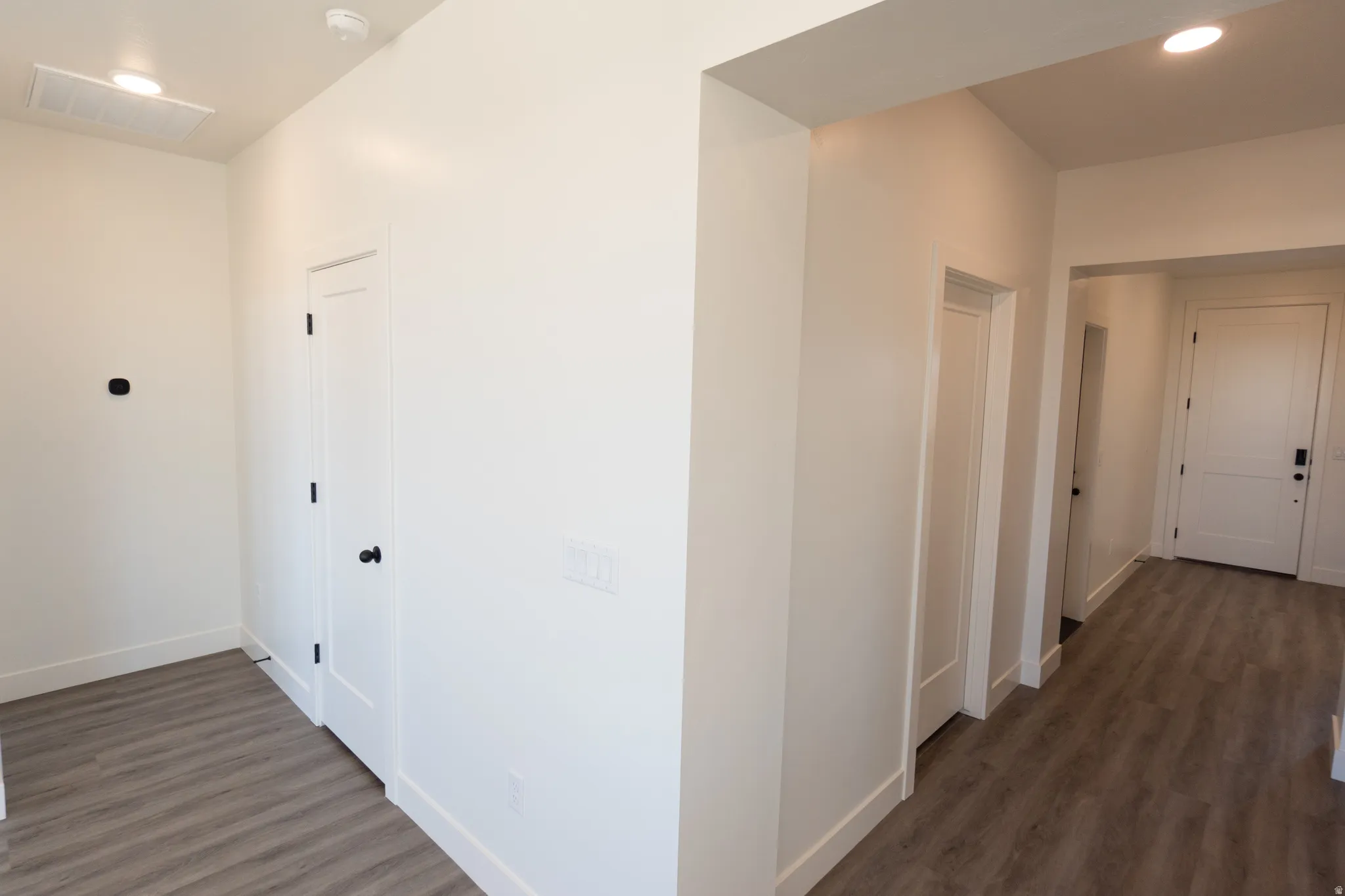 Wood-finish flooring, recessed lighting, and white interior doors with dark hardware