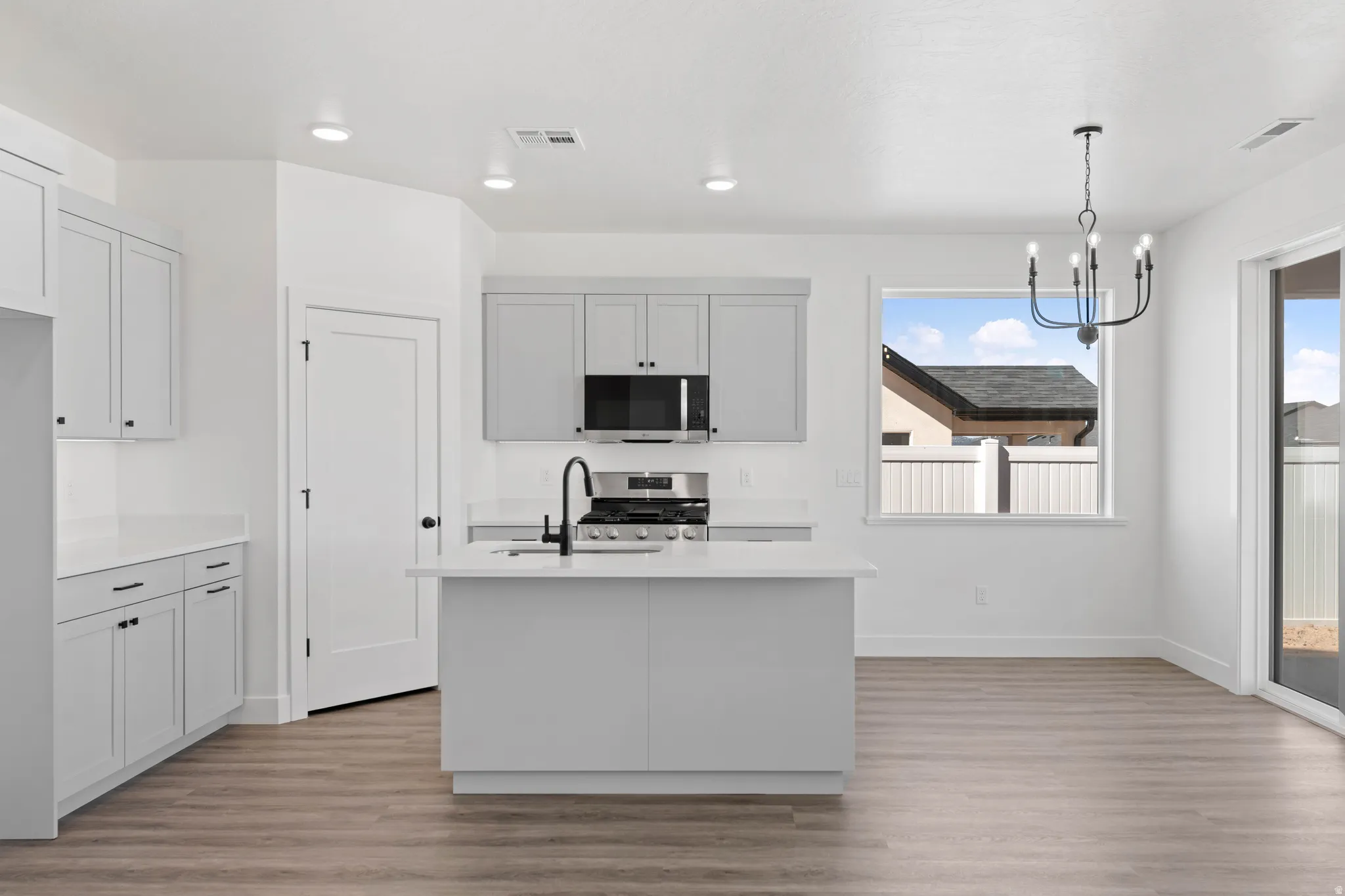 Modern kitchen featuring light gray cabinetry, a central island, stainless steel appliances, and wood-finish flooring
