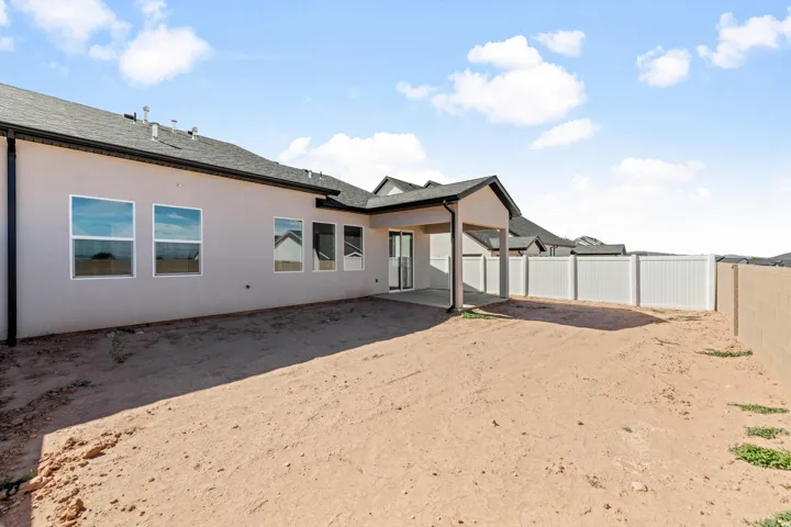 Expansive rear yard with a covered patio, multiple windows, and a vinyl privacy fence