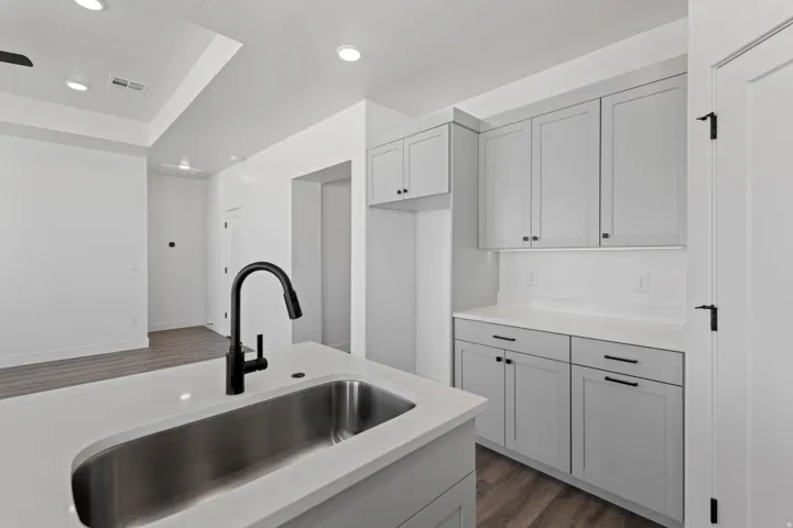 Kitchen area featuring light gray cabinetry, white countertops, a stainless steel sink, and a matte black gooseneck faucet