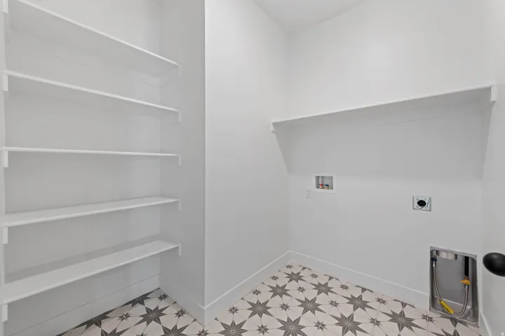 Laundry area featuring patterned floor tiles, white walls, built-in shelving, and utility hookups