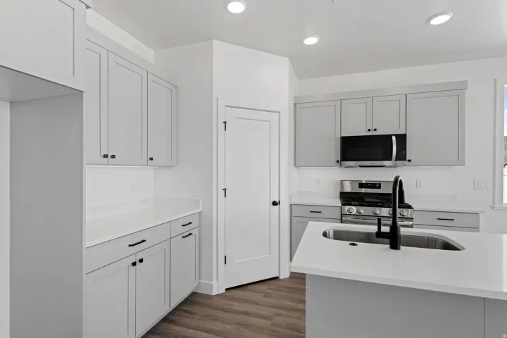 Contemporary kitchen featuring light gray cabinetry, white countertops, stainless steel appliances, and wood-finish flooring