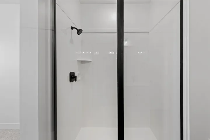 Shower enclosure with black-framed glass, white shower surround, matte black shower head, and matte black shower control