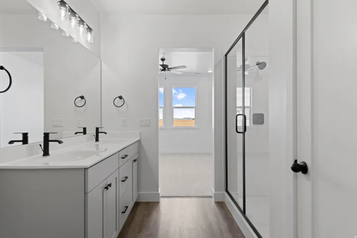 Dual vanity with matte black fixtures, framed glass shower enclosure, wood-finish flooring, and ample natural light