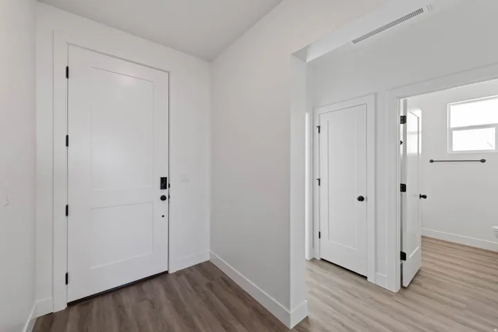 White interior doors, wood-finish flooring, matte black door hardware, white walls, and a window with natural light