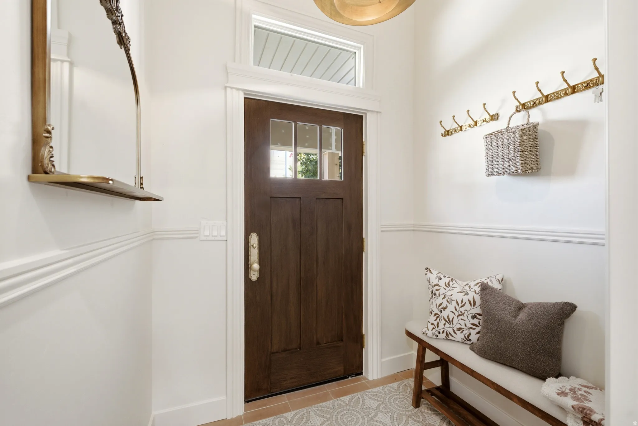Wood-paneled entry door with transom window, decorative wall molding, and tile flooring with a patterned inlay
