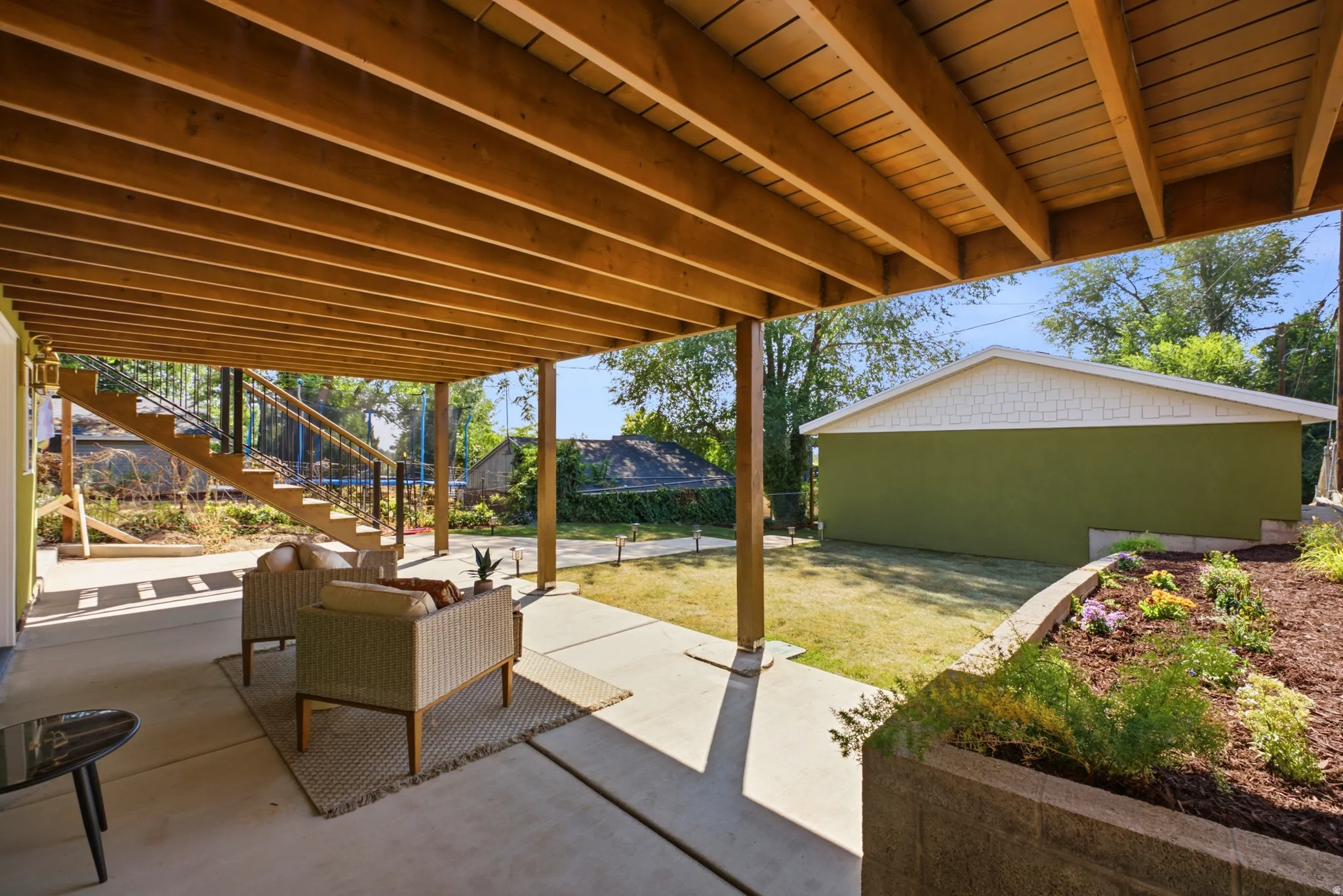 Expansive concrete patio with an exposed wood beam ceiling, leading to a wood staircase with black railings