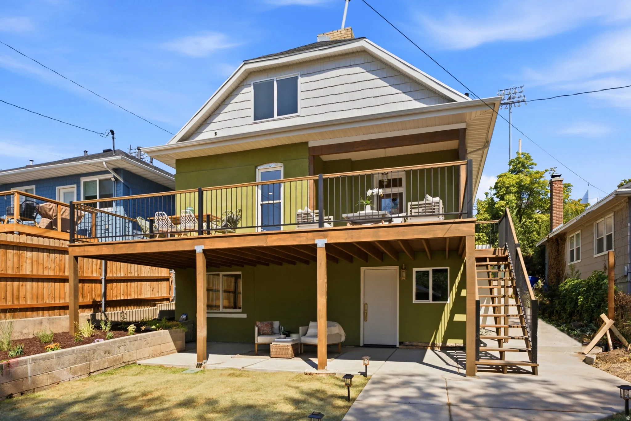 Modern home featuring a spacious covered deck with wood-beam construction, expansive lawn with mature landscaping, multi-level design with upper and lower living spaces, composite or wood-finish siding exterior, and integrated outdoor entertaining areas w