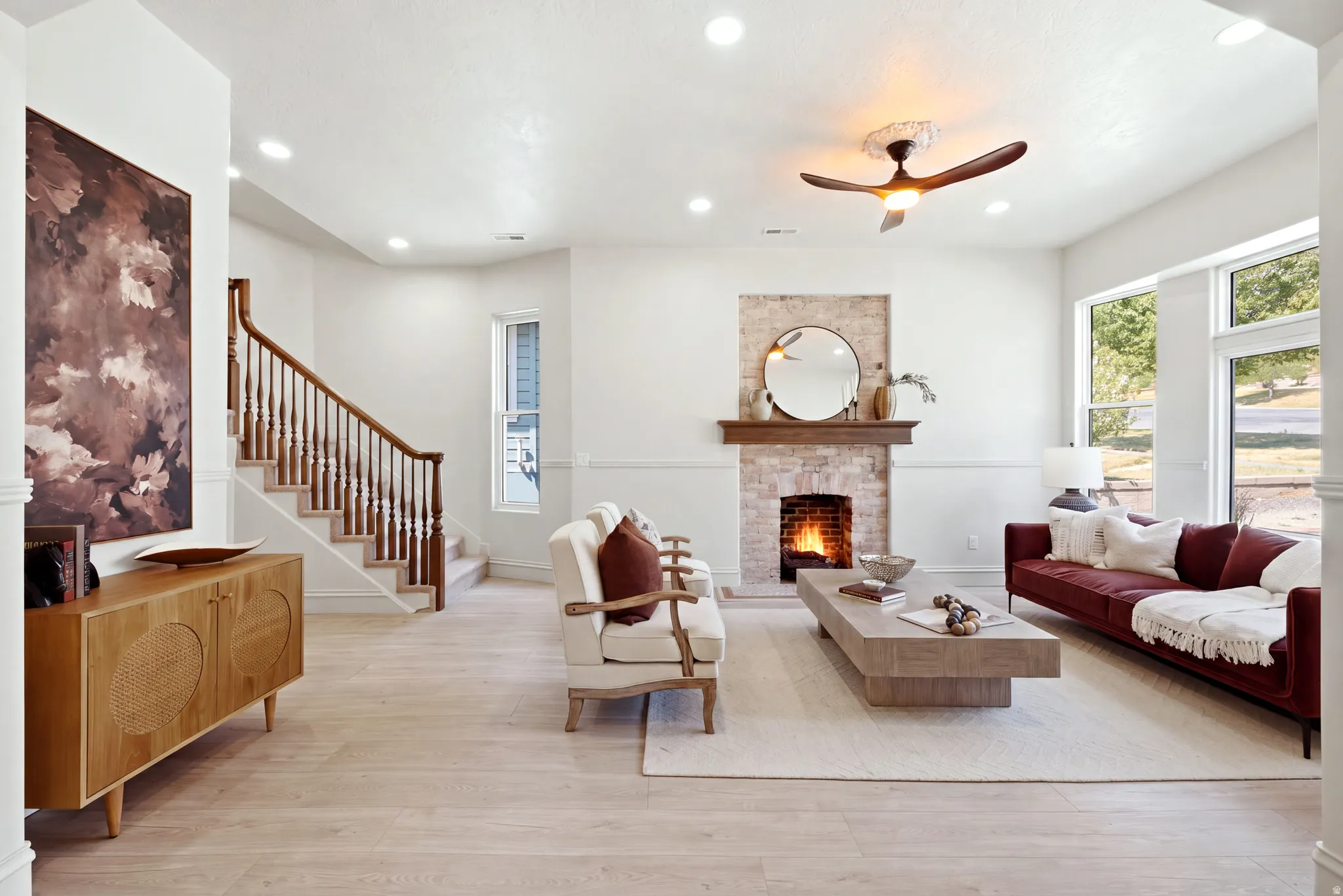 Recessed lighting, wood-finish flooring, brick fireplace with wood mantel, large windows, and an open baluster staircase