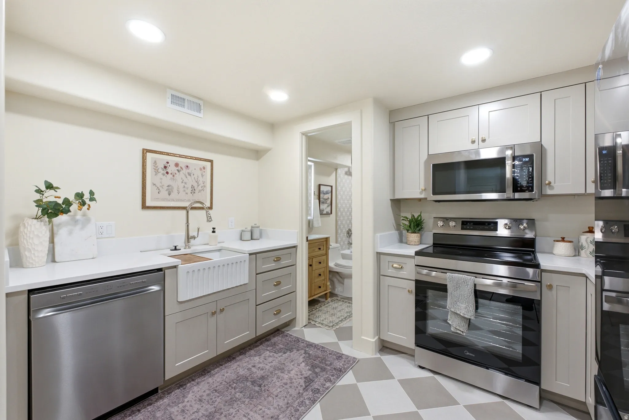 Stainless steel appliances, solid surface countertops, light-toned cabinetry, recessed lighting, and a farmhouse-style sink