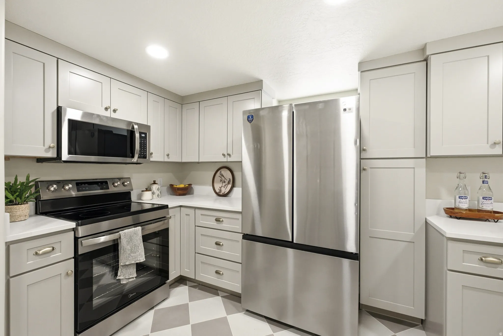 Stainless steel appliances, white countertops, shaker-style cabinetry, recessed lighting, and checkered flooring