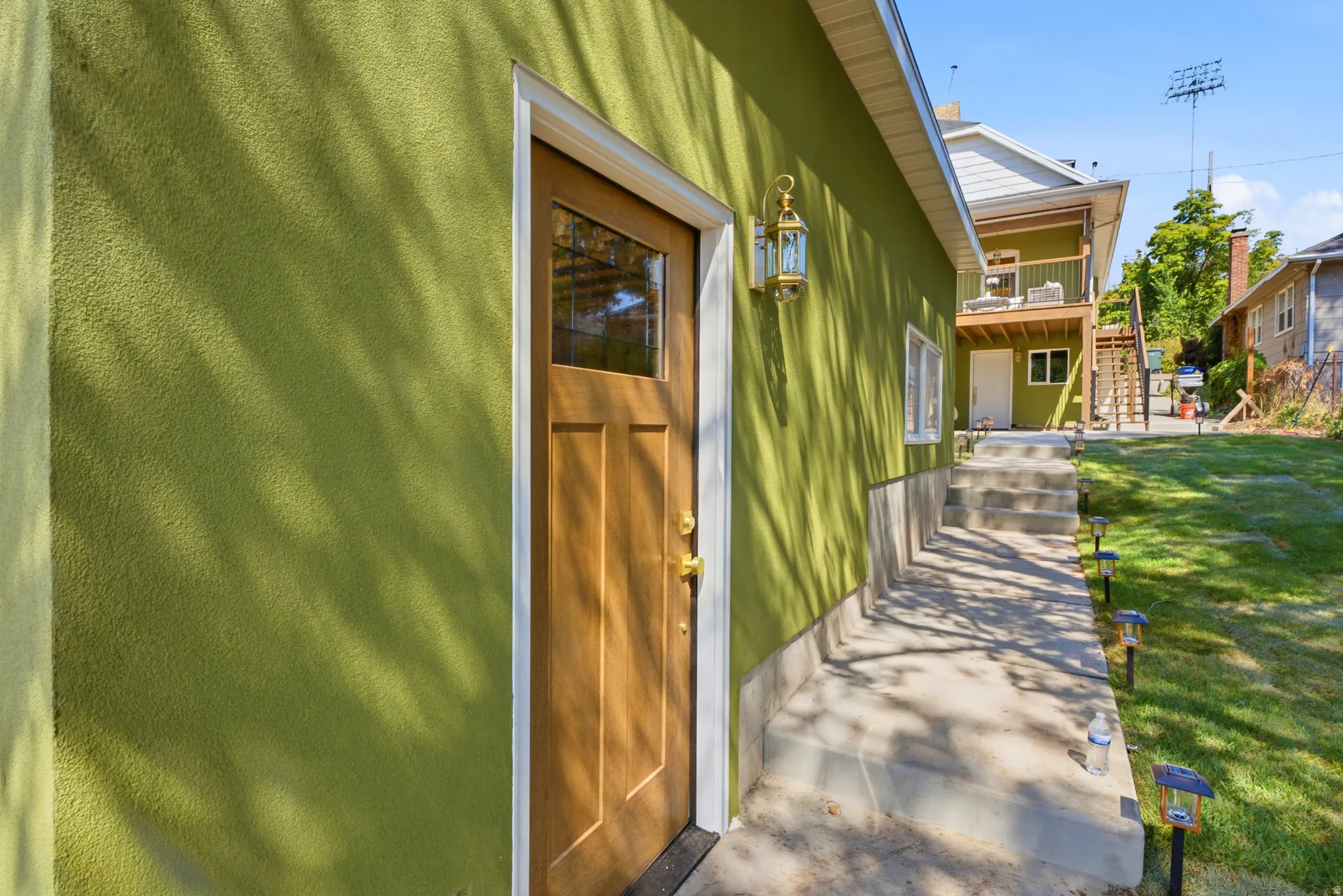 Stucco exterior with a wood-finish door and transom window, featuring an exterior wall lantern