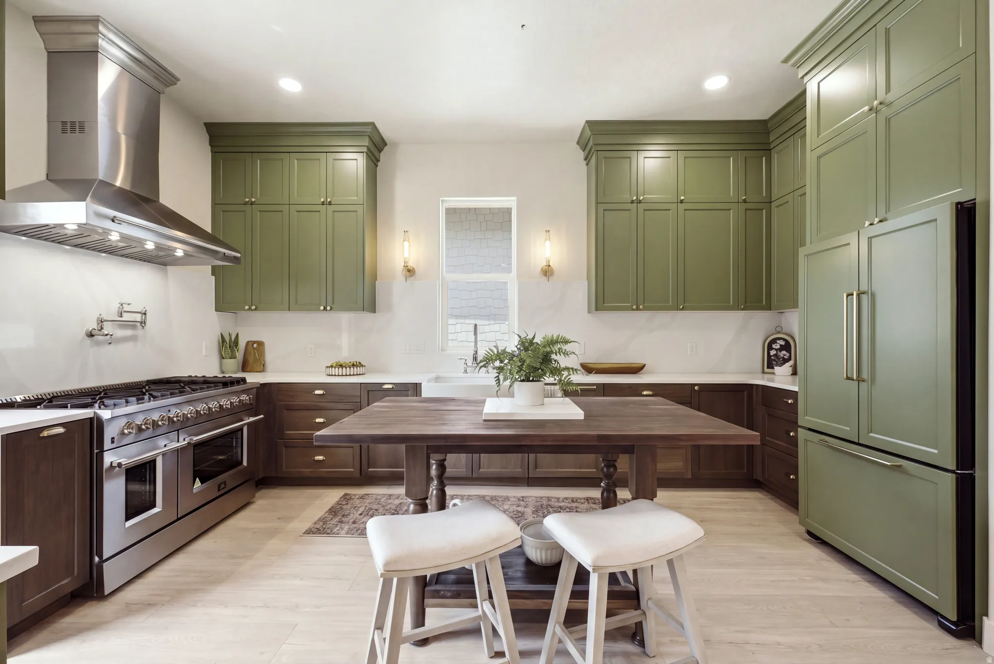 Gourmet kitchen featuring a stainless steel professional range with a matching range hood, custom green upper cabinetry, dark wood-finish lower cabinetry, and light wood-finish flooring