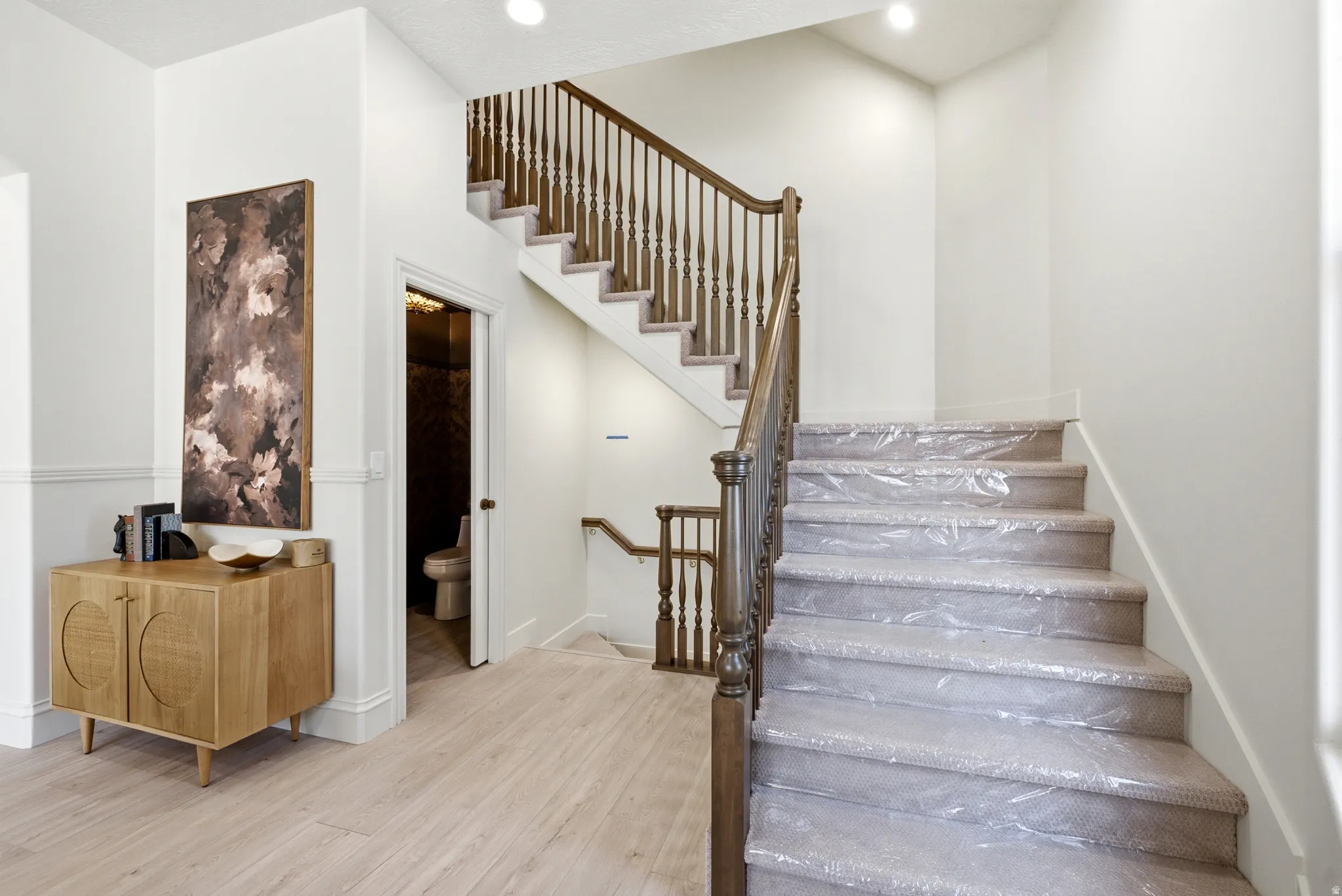 Hardwood flooring in a light finish, wainscoting, a wood staircase with balusters, and recessed lighting