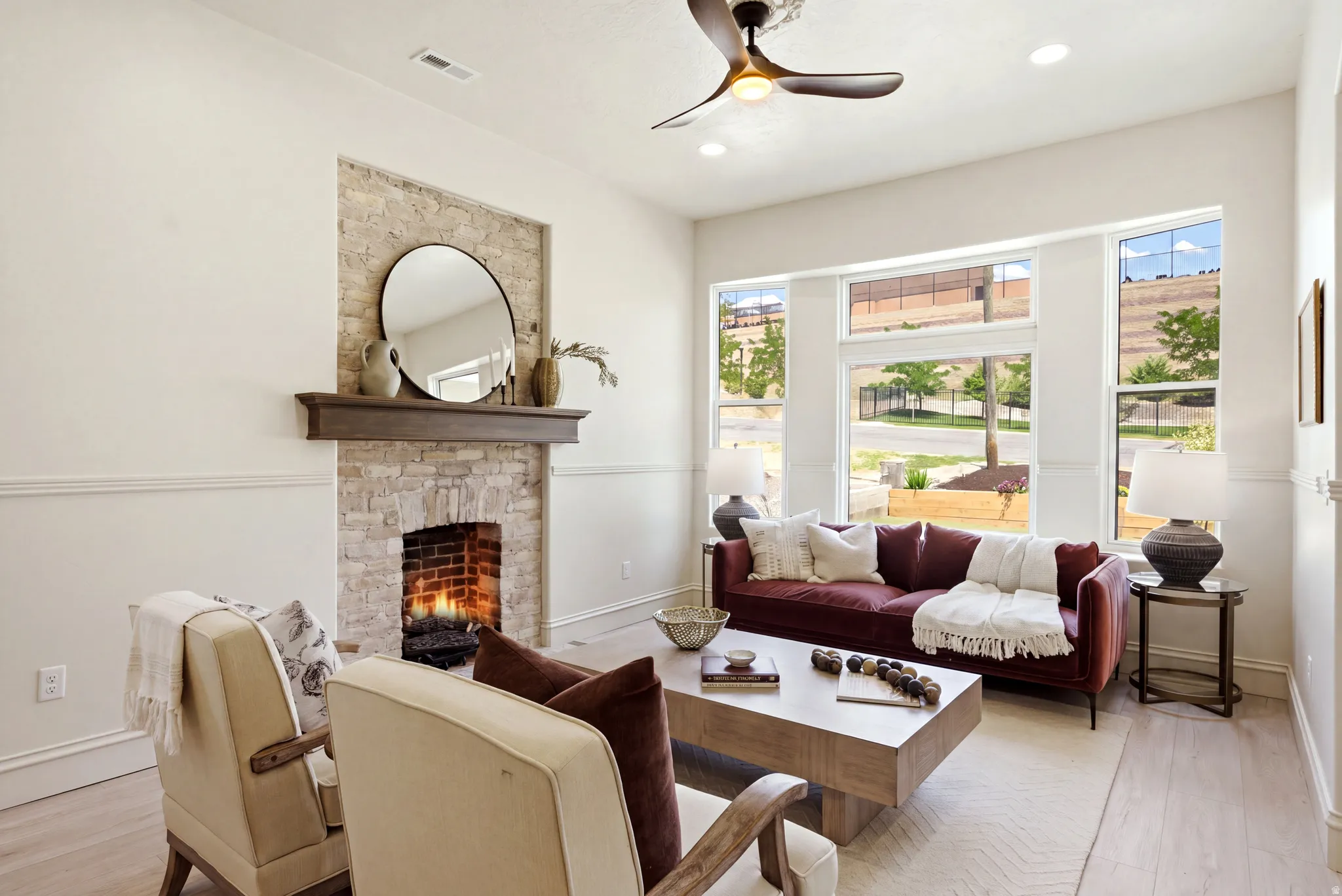 Stone-clad fireplace with wood mantel, large multi-pane windows, recessed lighting, and wood-finish flooring