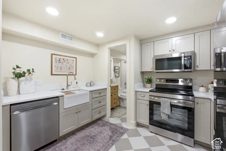 Stainless steel appliances, solid surface countertops, light-toned cabinetry, recessed lighting, and a farmhouse-style sink