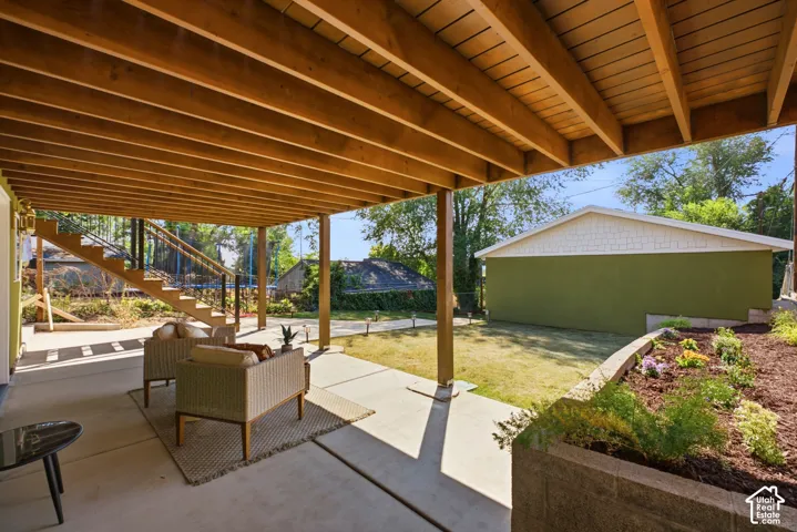 Expansive concrete patio with an exposed wood beam ceiling, leading to a wood staircase with black railings