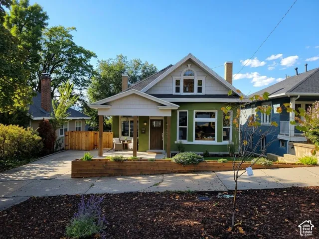 Gable roofline with arched window and decorative trim, covered porch with columns, stucco exterior with bay window, wood fence, and paved driveway