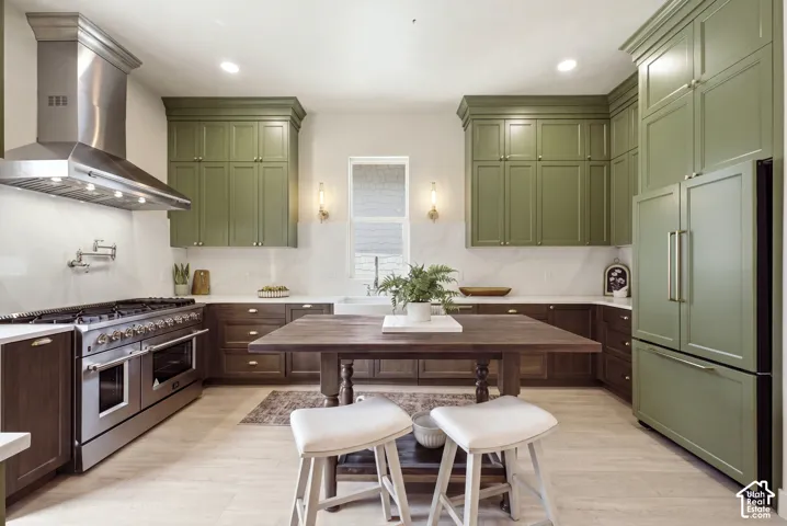 Gourmet kitchen featuring a stainless steel professional range with a matching range hood, custom green upper cabinetry, dark wood-finish lower cabinetry, and light wood-finish flooring