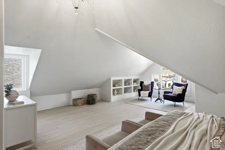 Sloped ceilings with a chandelier, wood-finish flooring, built-in shelving, and multiple windows with natural light