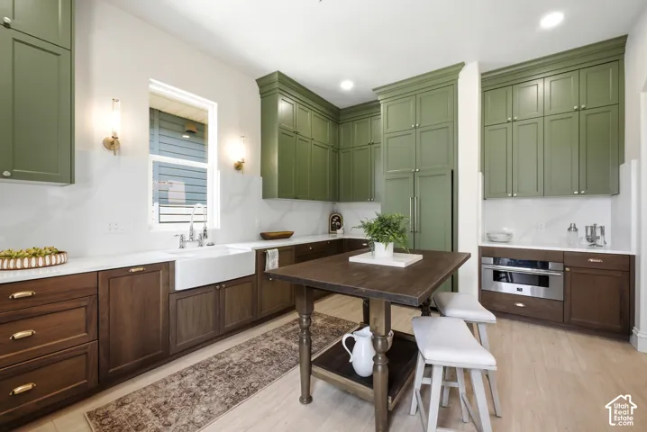 Kitchen featuring two-tone cabinetry, white countertops, an apron-front sink with a gooseneck faucet, and light wood-finish flooring