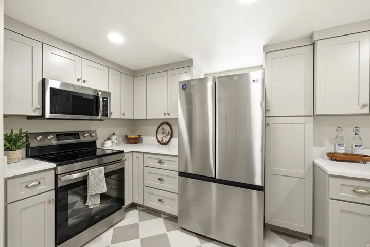 Stainless steel appliances, white countertops, shaker-style cabinetry, recessed lighting, and checkered flooring