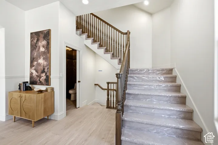 Hardwood flooring in a light finish, wainscoting, a wood staircase with balusters, and recessed lighting