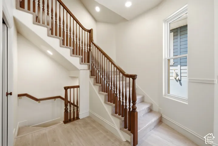 Hardwood handrails with turned wood balusters, carpeted stairs, recessed lighting, and wood-finish flooring