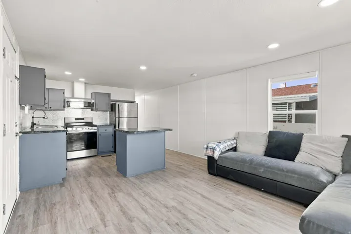 Open-concept living space with wood-finish flooring, recessed lighting, and a kitchen featuring stainless steel appliances, grey cabinetry, and a peninsula with countertop seating
